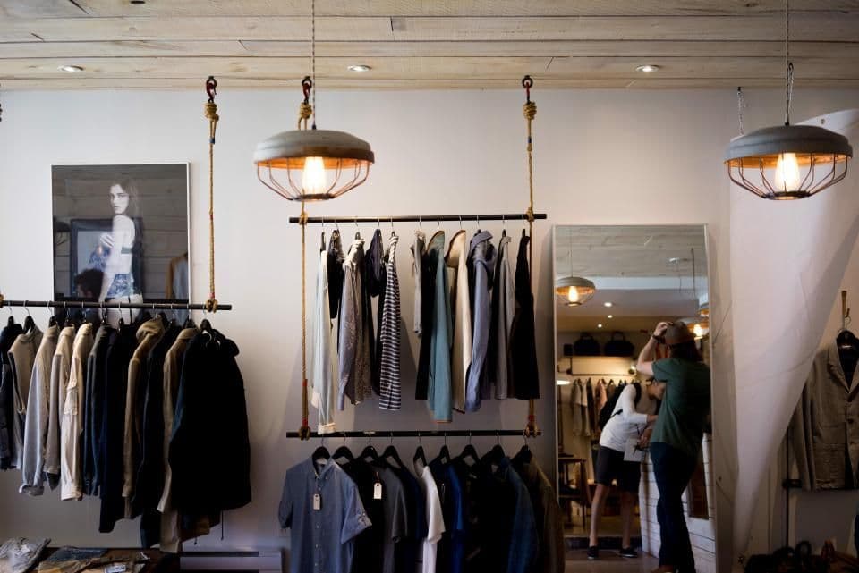 A small retail shop interior with clothing on rails under warm pendant lighting